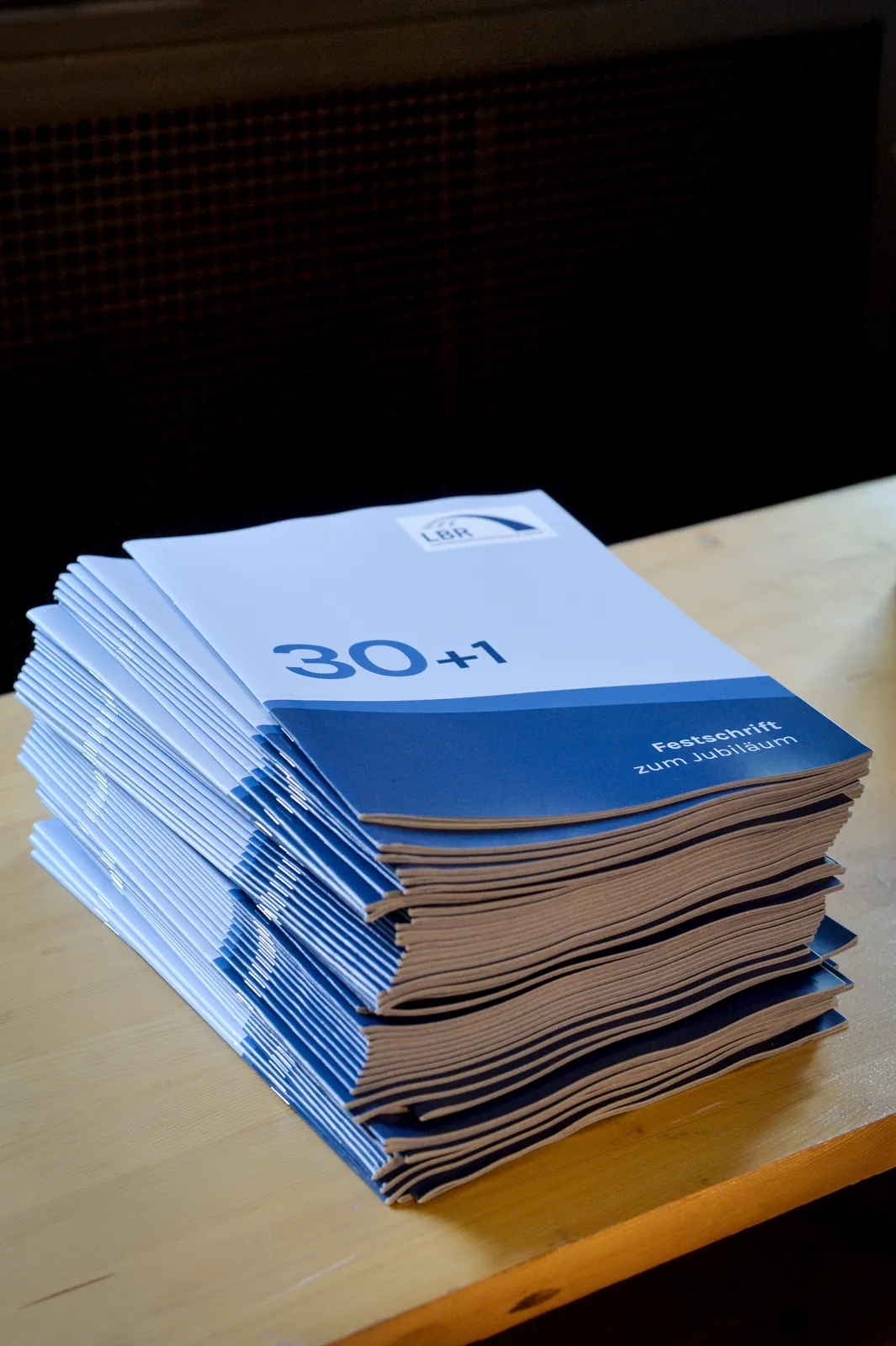 Ein Stapel gedruckter Festschriften „30+1“ liegt auf einem Tisch bereit.