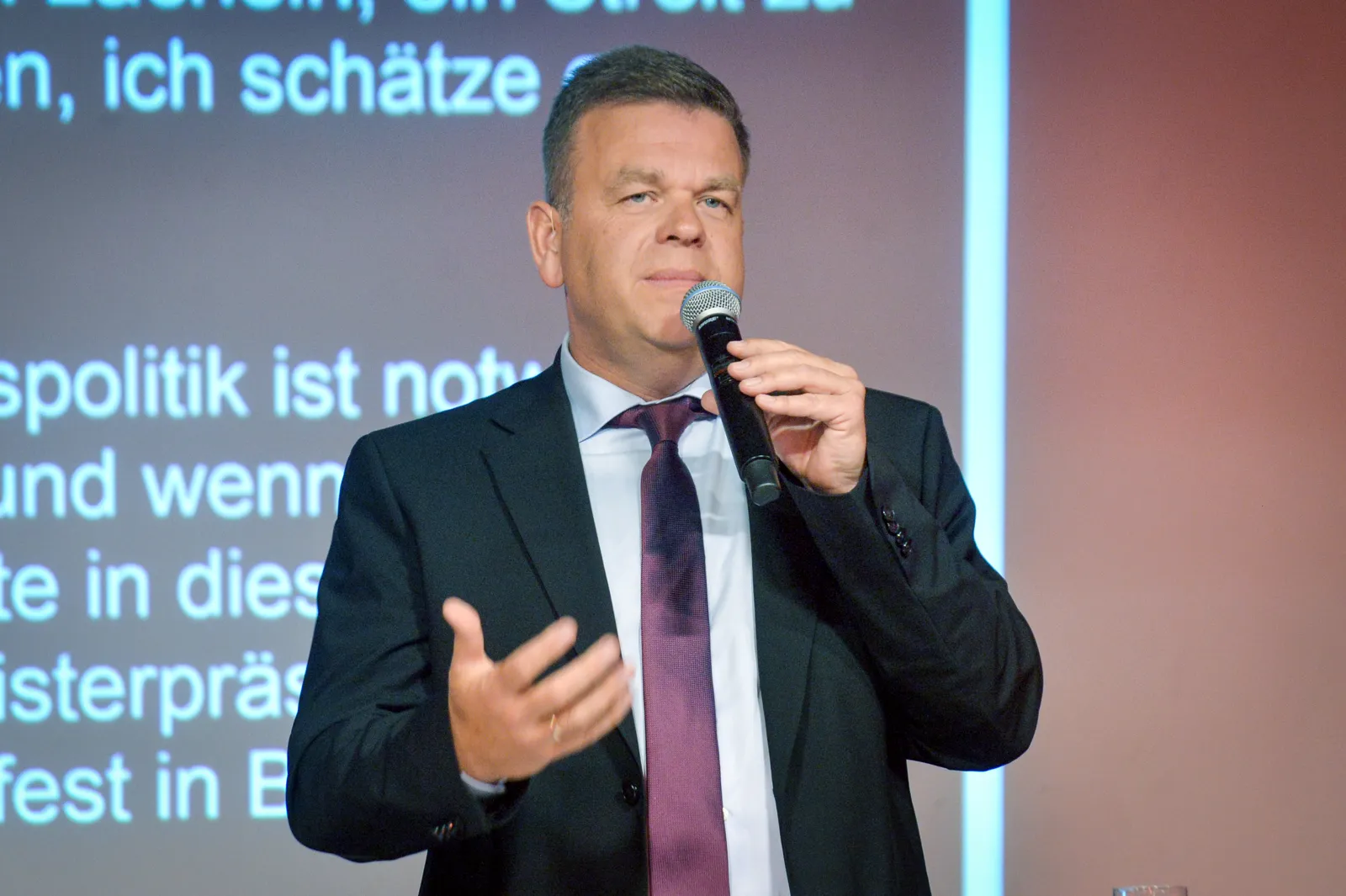 Staatssekretär Matthias Heidmeier spricht mit Mikrofon zu den Gästen der Jubiläumsfeier.